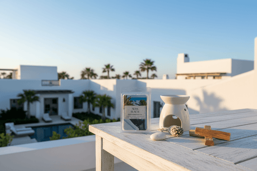 Alys Beach Soy Wax Melt 2.5 Oz 6-piece clamshell on a patio table with a wax warmer, set against a coastal villa backdrop for a spa-like ambiance.