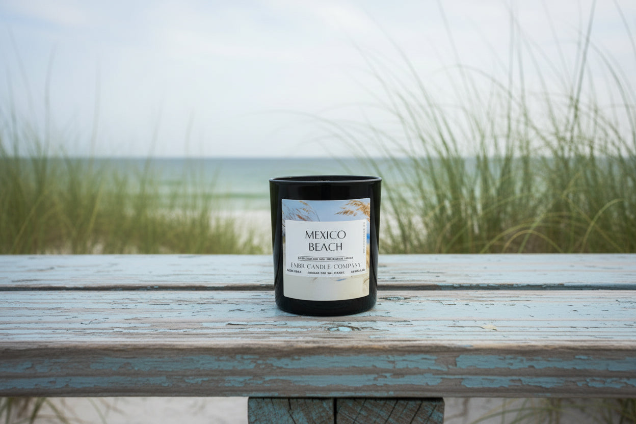Mexico Beach - Emerald Coast Collection - Soy Wax Candle in black glass jar on a weathered beachside bench with sea grass and ocean in background.